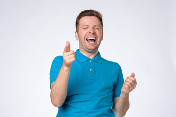 Sticker - Handsome young man laughing at joke with folded hands. Studio shot