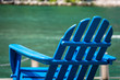 A blue wooden lawn chair on the waterfront riverwalk on a sunny day.