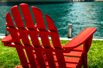 A red wooden lawn chair on the waterfront riverwalk on a sunny day.