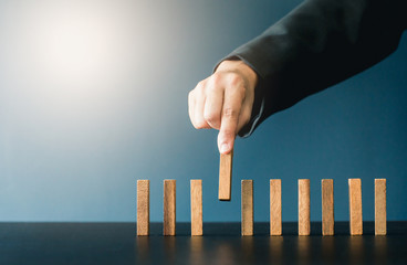 Close up of businessgirl hand Stopping Falling wooden Dominoes effect from continuous toppled or risk, strategy and successful intervention concept for business.