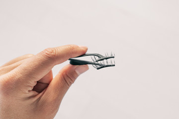 First person view of woman applying false magnetic eyelashes with metal applicator. Person holding pince to apply magnet fake lashes beauty trend.