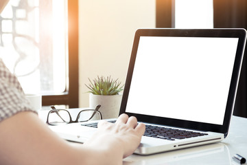 Man is typing on laptop computer keyboard which has white blank mock up screen.