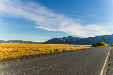 Perspective view of road trip on asphalt road with beautiful nature golden yellow grass and mountains in autumn in cloudy blue sky through national park south Patagonia, Argentina and Chile