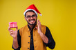 © yurakrasil - indian man wearing stylish traditional kurta great smile in santa hat with gift box on yellow background studio.dark-skinned Santa Claus congratulating merry christmas