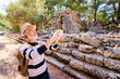 © luengo_ua - Enjoying travel. Senior man with backpack taking photo on smartphone on ancient sightseeing background