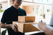 © wutzkoh - Delivery young man standing at the door of home and carrying parcels for young male to signing.