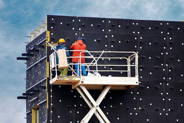 Canvas Print - External facade thermal insulation. Professional construction workers on scissor lift insulating wall facade with mineral wool for thermal protection. Workers wearing safety harness insulated wall