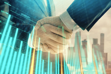 Double exposure of financial graph on cityscape background with two businessman handshake. Concept of stock market deal