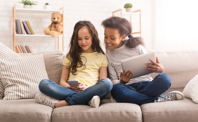 Wall Mural - Preteen girls with gadgets sitting on sofa at home