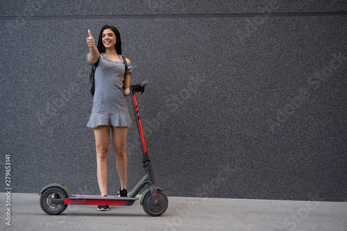 Fotografía Cute cheerful young woman next to electric scooter showing thumbs