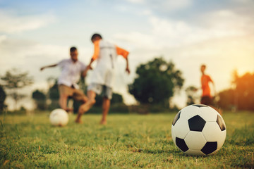 Action sport outdoors of kids having fun playing soccer football for exercise in community rural area under the twilight sunset sky. Fresh and vibrant image with anonymous people.