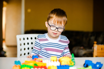 little boy in the glasses with syndrome dawn playing with colorful bricks