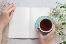 Woman Is Reading An Open Blank Page Book With A Copy Space And Drinking A Tea From A Cup On A Old White Wooden Table Background.