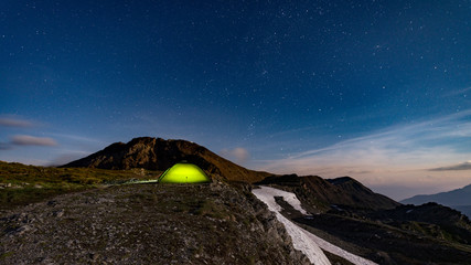 Wall Mural - panorama of illuminated green tent under starry night - fog rolling over mountains
