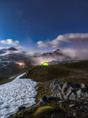 Wall Mural - moonlit scene with illuminated green tent under starry night - fog rolling over mountains