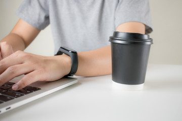Poster - Young hands wearing a gray T-shirt using a laptop with coffee in the office. Side view