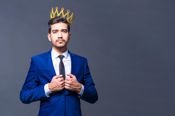 Attractive young man with a crown on his head on a gray background.