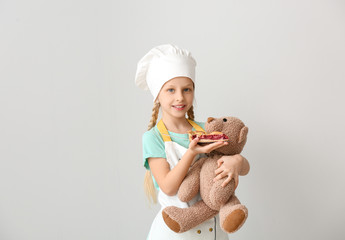 Sticker - Cute little chef feeding toy bear with piece of pie on white background