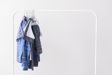 Stylish kid clothes hanging on rack against light background