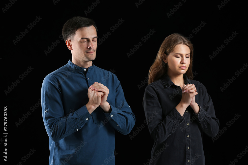Religious couple praying to God on dark background
