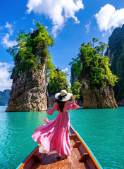 Wall Mural - Beautiful girl standing on the boat and looking to mountains in Ratchaprapha Dam at Khao Sok National Park, Surat Thani Province, Thailand.