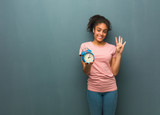 Fototapeta Łazienka - Young black woman showing number four. She is holding an alarm clock.