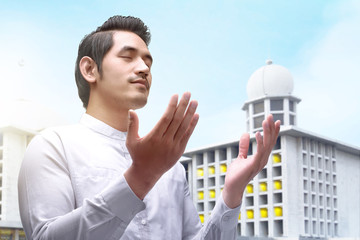 Wall Mural - Asian Muslim man standing and praying while raised arms