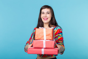 Wall Mural - Cheerful good looking young brunette woman holding a red gift boxes in her hands, but against a blue background. Concept holidays and presents