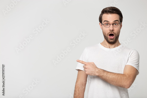 Fotomural Surprised young man wearing glasses pointing finger aside at copyspace