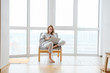 © sata_production - Woman in armchair working on laptop near panoramic window
