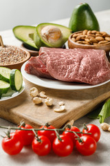 Wall Mural - raw meat on wooden chopping board near nuts and vegetables isolated on grey, ketogenic diet menu