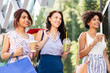 © Syda Productions - sale, consumerism and people concept - happy young women with shopping bags and drinks walking along city street