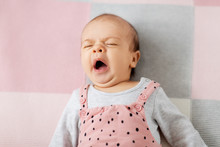 Babyhood And People Concept - Sweet Yawning Little Baby Girl In Pink Suit Lying On Knitted Blanket