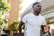 © twinsterphoto - African American man jogging in the city park. Young male fit person in white shirt running outdoors