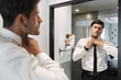 © Drobot Dean - Image closeup of handsome man wearing formal suit looking at mirror in bathroom at hotel room during business trip