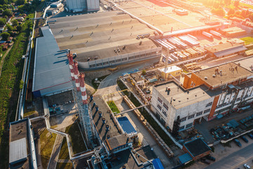 Wall Mural - Aerial view of industrial area with warehouses, factory buildings and chimney on foreground at sunset, drone photo