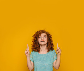 Looking higher. Woman with curls pointing hand up on yellow background