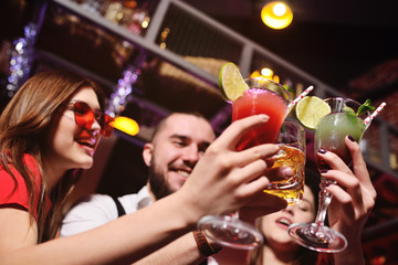 group of friends-young guy and two cute girls having fun at a party holding cocktails