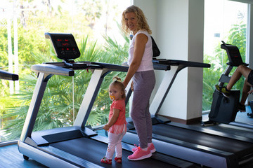 Mom with the child on the treadmill in the gym.