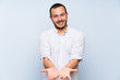 © luismolinero - Colombian man over isolated blue wall holding copyspace imaginary on the palm to insert an ad
