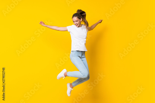 Fotografía Young woman jumping over isolated yellow wall