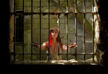 A Young Woman Prays Inside A Jail Ruin. She Is  Dressed In White And Wears A Thorn Wreath On  Her Head. 