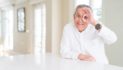 Poster - Handsome senior man at home doing ok gesture with hand smiling, eye looking through fingers with happy face.