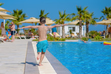 Smiling Caucasian Boy Having Fun In Swimming Pool At Resort On Family Vacation. He Is Running Along Pool Edge.