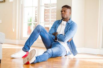 Poster - African american man wearing headphones listening to music sitting on the floor skeptic and nervous, disapproving expression on face with crossed arms. Negative person.