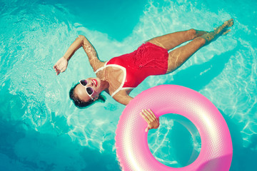 Enjoying suntan and vacation. Outdoor portrait of pretty young woman in red swimsuit with inflatable ring in swimming pool.