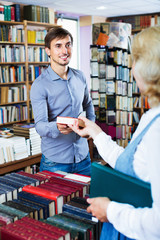 Wall Mural - Young smiling man taking chosen book from seller