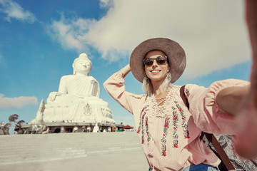 Traveling by Thailand. Pretty young woman in hat taking selfie in the Big Buddha Temple, famous Phuket sightseeing.