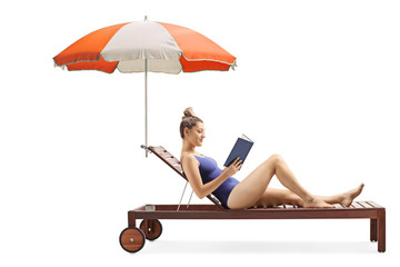 Wall Mural - Young woman reading a book and relaxing on a sunbed under umbrella