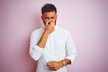 Canvas Print - Young indian businessman wearing elegant shirt standing over isolated pink background smelling something stinky and disgusting, intolerable smell, holding breath with fingers on nose. Bad smells 